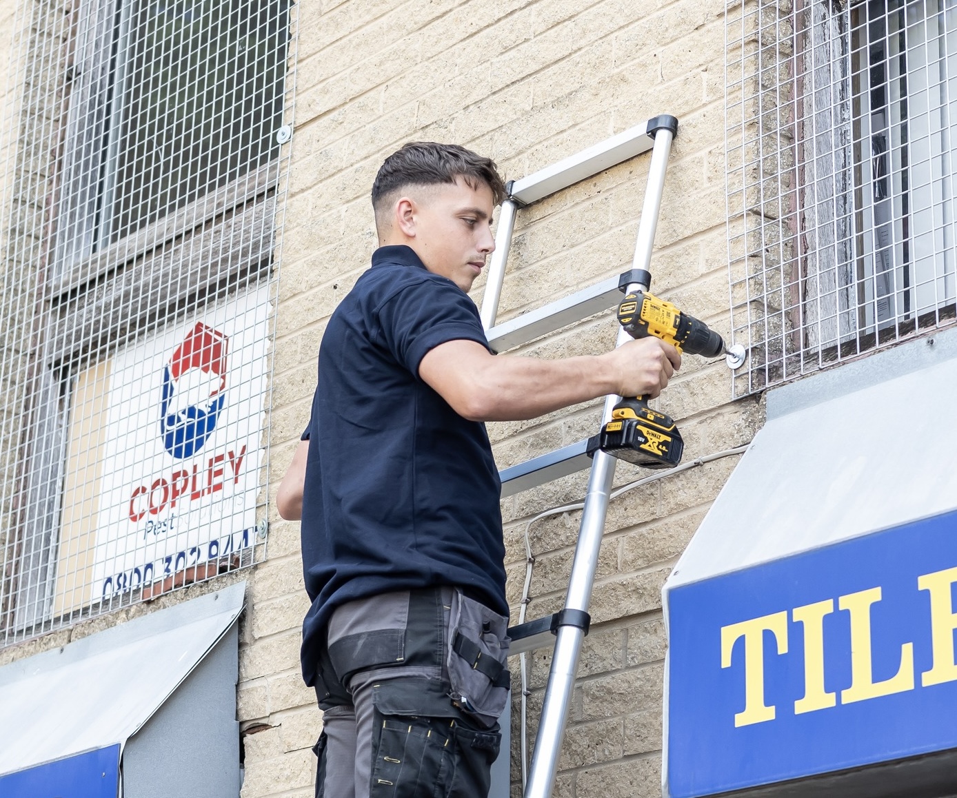A Copley Pest Controller on a ladder above a commercial building